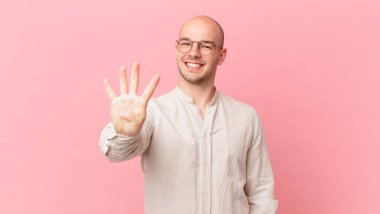 Kel adam gülümsüyor ve arkadaş canlısı görünüyor, 4 ya da 4 numarayı gösteriyor, eli önde, geriye doğru sayıyor.