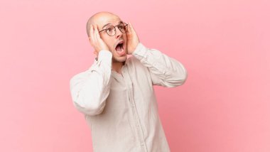 Kel adam mutlu, heyecanlı ve şaşırmış hissediyor, iki eli yüzü de havada bir tarafa bakıyor.