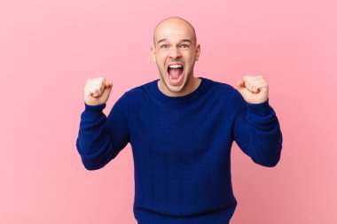 Kel adam öfkeli bir ifadeyle ya da yumruklarıyla başarıyı kutlarken agresif bir şekilde bağırıyor.