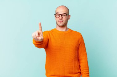 Kel adam gururla gülümsüyor ve gururla bir numaralı pozunu veriyor, kendini lider gibi hissediyor.