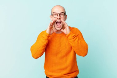 Kel adam mutlu, heyecanlı ve pozitif hissediyor. Elleri ağızda, bağırarak bağırıyor.