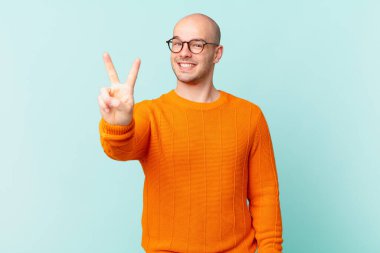 Kel adam gülümsüyor ve arkadaş canlısı görünüyor, iki ya da iki numarayı gösteriyor, eli önde, geriye doğru sayıyor.