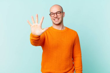 Kel adam gülümsüyor ve dost canlısı görünüyor. 5 ya da 5 numarayı gösteriyor. Eli önde, geriye doğru sayıyor.