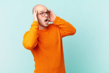 Kel adam mutlu, heyecanlı ve şaşırmış hissediyor, iki eli yüzü de havada bir tarafa bakıyor.