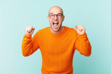 Kel adam öfkeli bir ifadeyle ya da yumruklarıyla başarıyı kutlarken agresif bir şekilde bağırıyor.