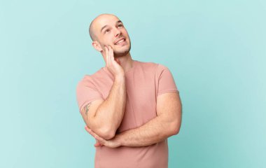 Kel adam mutlu bir şekilde gülümsüyor ve hayal kuruyor ya da şüphe ediyor.