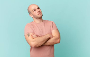 Kel adam omuz silkiyor, kafası karışık ve kararsız, kolları bağlı ve şaşkın bir şekilde şüpheye düşmüş görünüyor.