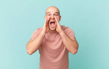 Kel adam mutlu, heyecanlı ve pozitif hissediyor. Elleri ağızda, bağırarak bağırıyor.