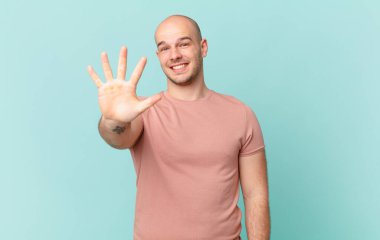 Kel adam gülümsüyor ve dost canlısı görünüyor. 5 ya da 5 numarayı gösteriyor. Eli önde, geriye doğru sayıyor.