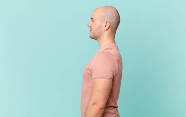 Kel adam profil görünümünde. İlerideki boşluğu kopyalamak istiyor. Düşünüyor, hayal ediyor ya da hayal ediyor.