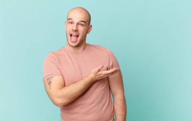 Kel adam mutlu bir şekilde gülümsüyor, mutlu hissediyor ve fotokopi alanında avucuyla bir konsept gösteriyor.