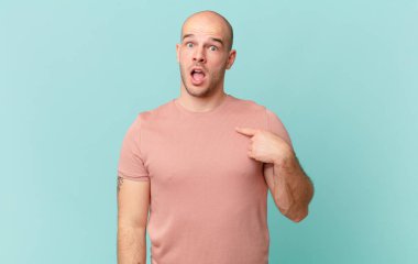 Şok olmuş ve ağzı açık, kendini işaret eden kel bir adam.