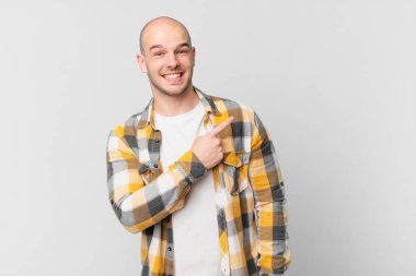 Kel adam neşeyle gülümsüyor, mutlu hissediyor ve kenarı ve yukarıyı işaret ediyor, fotokopi alanında nesneler gösteriyor.