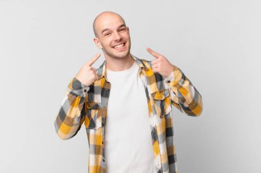 Kel adam kendine güvenerek gülümsüyor. Geniş gülüşünü gösteriyor. Olumlu, rahat, tatmin olmuş bir tavır.