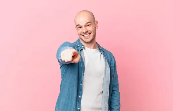 bald man pointing at camera with a satisfied, confident, friendly smile, choosing you