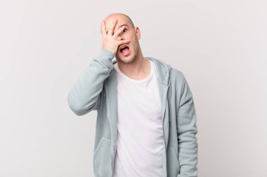 Kel adam şok olmuş, korkmuş ya da korkmuş görünüyor. Yüzü elle örtülmüş ve parmaklarının arasından gizlice bakıyor.