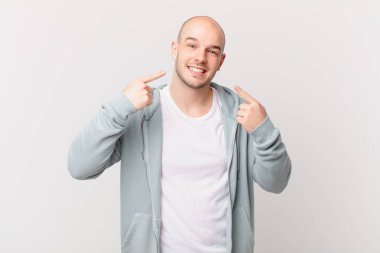 Kel adam kendine güvenerek gülümsüyor. Geniş gülüşünü gösteriyor. Olumlu, rahat, tatmin olmuş bir tavır.