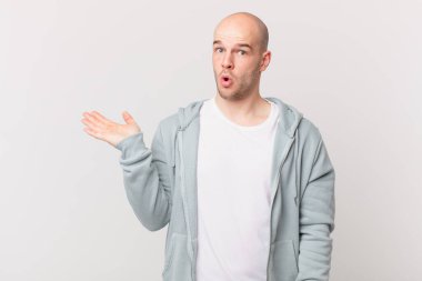 Kel adam şaşırmış ve şoka uğramış görünüyor, çenesi düşmüş ve eli açık bir nesneyi tutuyor.