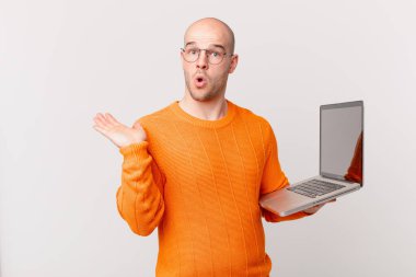 Bilgisayarlı kel adam şaşırmış ve şoka uğramış görünüyor, çenesi düşmüş ve eli açık bir nesneyi tutuyor.