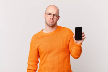 Akıllı telefonlu kel bir adam üzgün ve mızmız, mutsuz bir bakışla, olumsuz ve hayal kırıklığına uğramış bir tavırla ağlıyor.