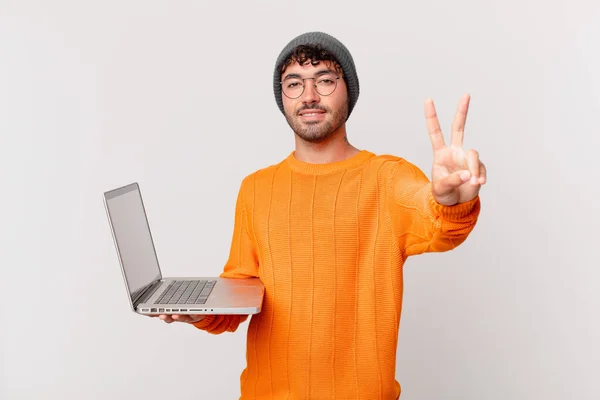コンピュータを持っているオタクの男は笑顔で友好的に見えます前方に手で2番目または2番目を示します — ストック写真
