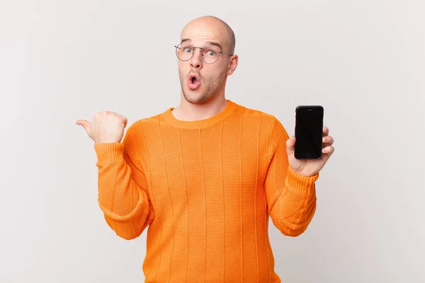 光秃秃的男人拿着智能手机 带着怀疑的表情 指着旁边的物体说 难以置信 — 图库照片