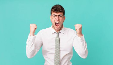 Genç işadamı öfkeli bir ifadeyle ya da yumruklarıyla başarıyı kutlarken agresif bir şekilde bağırıyor.