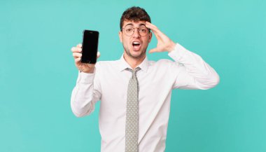 Akıllı telefonlu bir iş, mutlu, şaşkın ve şaşırmış görünüyor, gülümsüyor ve inanılmaz ve inanılmaz iyi haberleri fark ediyor.