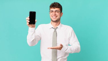 Akıllı telefonlu bir iş. Neşeli bir şekilde gülümsüyor, mutlu hissediyor ve fotokopi alanında avuç içiyle bir konsept gösteriyor.