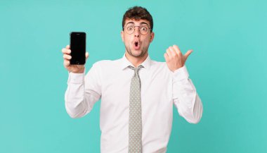 Akıllı telefonlu bir işletme, inançsızlığa hayret ediyor, yan taraftaki objeyi işaret ediyor ve 