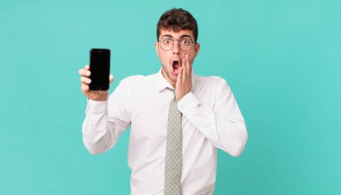 Akıllı telefonlu bir iş. Şok olmuş ve korkmuş. Ağzı açık ve elleri yanaklarında.