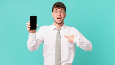 Akıllı telefonlu bir iş. Şok olmuş ve şaşırmış görünüyor. Ağzın sonuna kadar açık, kendini gösteriyorsun.