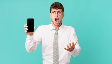 Akıllı telefonlu bir iş son derece şaşırmış, şaşırmış, endişeli ve paniklemiş, stresli ve dehşete kapılmış bir bakışla