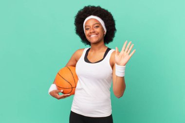 Afro kadın mutlu ve neşeli bir şekilde gülümsüyor, el sallıyor, seni selamlıyor ve selamlıyor, ya da veda ediyor. Basketbol konsepti