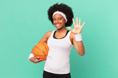 Afro kadın gülümsüyor ve arkadaş canlısı görünüyor. 5 ya da 5 numarayı gösteriyor. Eli önde, geriye doğru sayıyor. Basketbol konsepti