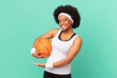 Afro kadın neşeyle gülümsüyor, kendini mutlu hissediyor ve fotokopi uzayda avucuyla bir konsept gösteriyor. Basketbol konsepti