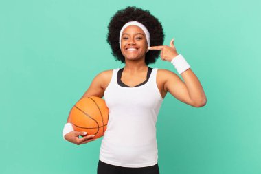 Afro kadın kendi geniş gülüşünü, pozitif, rahat, tatmin olmuş tavrını, kendine gülerek gösteriyor. Basketbol konsepti