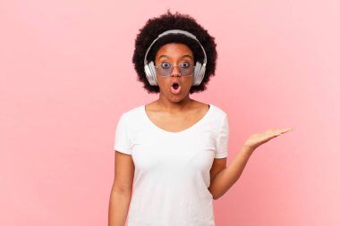 Afro kadın şaşırmış ve şok olmuş görünüyor. Çenesi düşmüş ve eli açık bir objeyi tutuyor. müzik konsepti