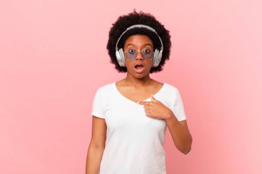 Afro kadın şok olmuş ve ağzı açık, kendini işaret ederek şaşırmış görünüyor. müzik konsepti
