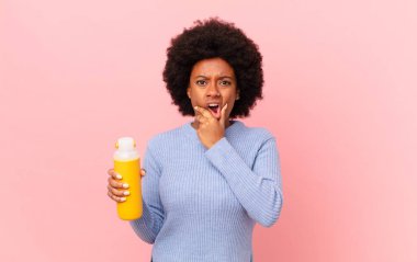 Ağzı ve gözleri açık, eli çenesinde olan afro bir kadın, hoş olmayan bir şok geçiriyor, ne ya da vay canına diyor. pürüzsüz konsept