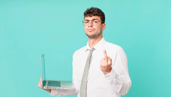 businessman with laptop feeling angry, annoyed, rebellious and aggressive, flipping the middle finger, fighting back