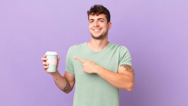 Kahveli adam neşeyle gülümsüyor, mutlu hissediyor ve yan ve yukarı doğru işaret ediyor, fotokopi alanında nesneler gösteriyor.