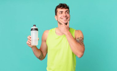 Fitness adamı mutlu bir şekilde gülümsüyor ve hayal kuruyor ya da şüphe ediyor, yana bakıyor.