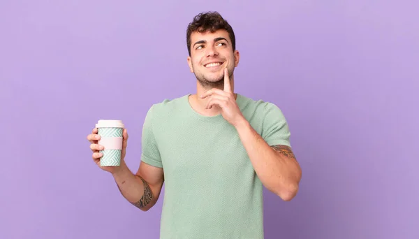 Mężczyzna Kawą Uśmiechający Się Szczęśliwie Marzący Lub Wątpiący Spoglądający Bok — Zdjęcie stockowe