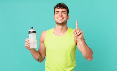 Fitness adamı gülümsüyor ve arkadaş canlısı görünüyor, bir numarayı gösteriyor ya da ilk eli önde, geri sayıyor.