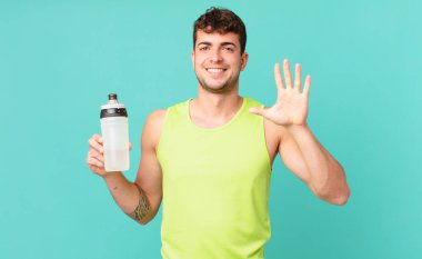 Fitness adamı gülümsüyor ve arkadaş canlısı görünüyor, 5 ya da 5 numarayı gösteriyor, eli önde, geriye doğru sayıyor.
