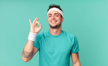 Fitness adamı mutlu, rahat ve tatmin olmuş hissediyor. Onayını iyi bir hareketle gösteriyor. Gülümsüyor.