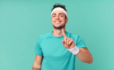Fitness adamı gururla gülümsüyor ve gururla bir numaralı pozu veriyor, kendini lider gibi hissediyor.