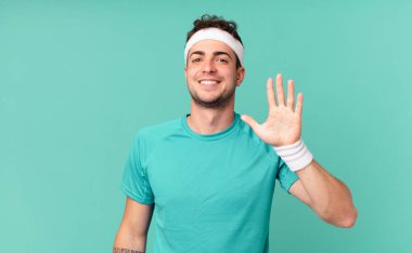 Fitness adamı gülümsüyor ve arkadaş canlısı görünüyor, 5 ya da 5 numarayı gösteriyor, eli önde, geriye doğru sayıyor.