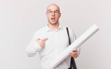 Mimar şaşkın ve şaşkın görünüyor, ağzı açık, kendini işaret ederek.